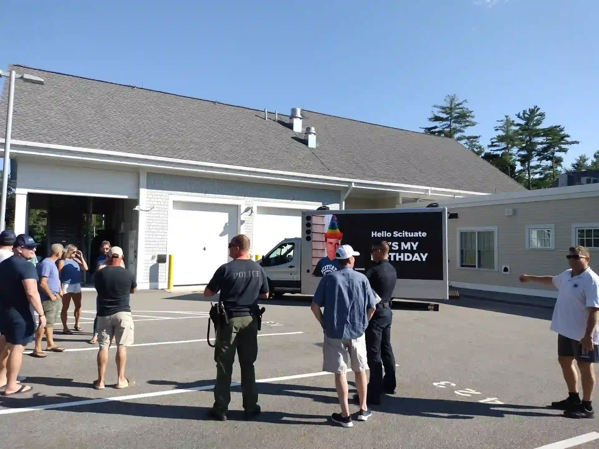 Birthday group and Scituate police officers gathered around an LED billboard truck displaying a birthday surprise message in Scituate Massachusetts