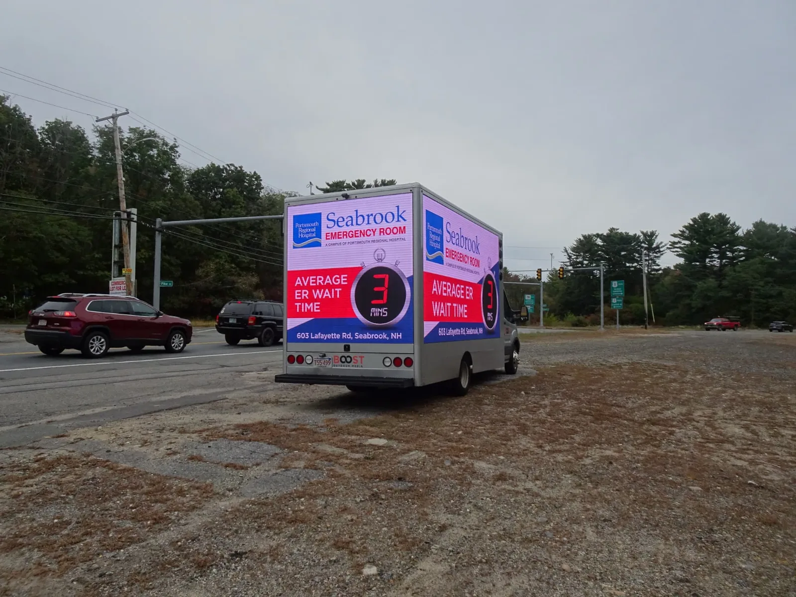 LED billboard truck with three screens showing Seabrook Emergency Room average ER wait time of 3 minutes at a busy roadside intersection in New Hampshire