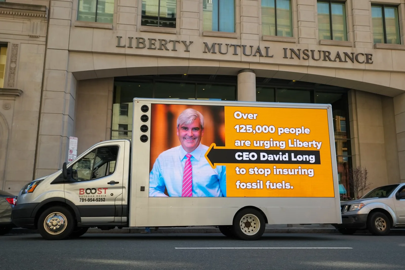 Mobile LED billboard truck running a fossil fuel accountability ad outside a Boston insurance headquarters
