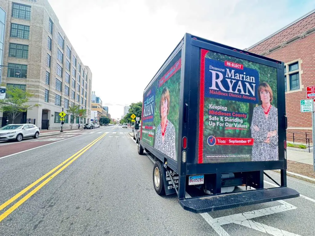 Rear LED screen of a Boost Outdoor Media mobile billboard truck displaying the Marian Ryan for Middlesex District Attorney campaign ad on a city street