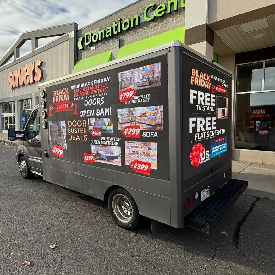 Mobile LED billboard truck showing furniture special offers and free TV promotion at a retail plaza
