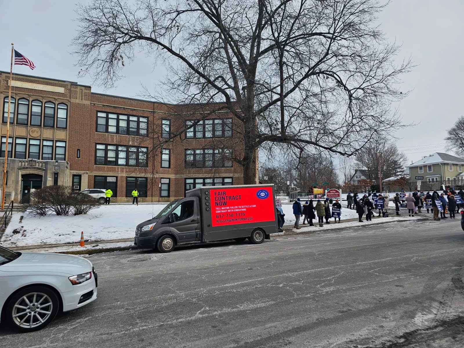 Teachers union LED billboard truck parked outside the Newton Education Center with educators picketing on the sidewalk