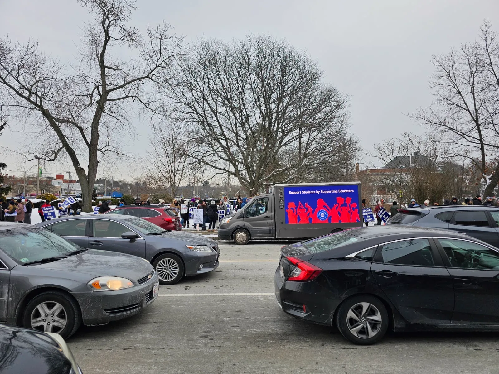 LED billboard truck displaying Support Students by Supporting Educators beside a teachers union rally with picket signs in Newton, Massachusetts