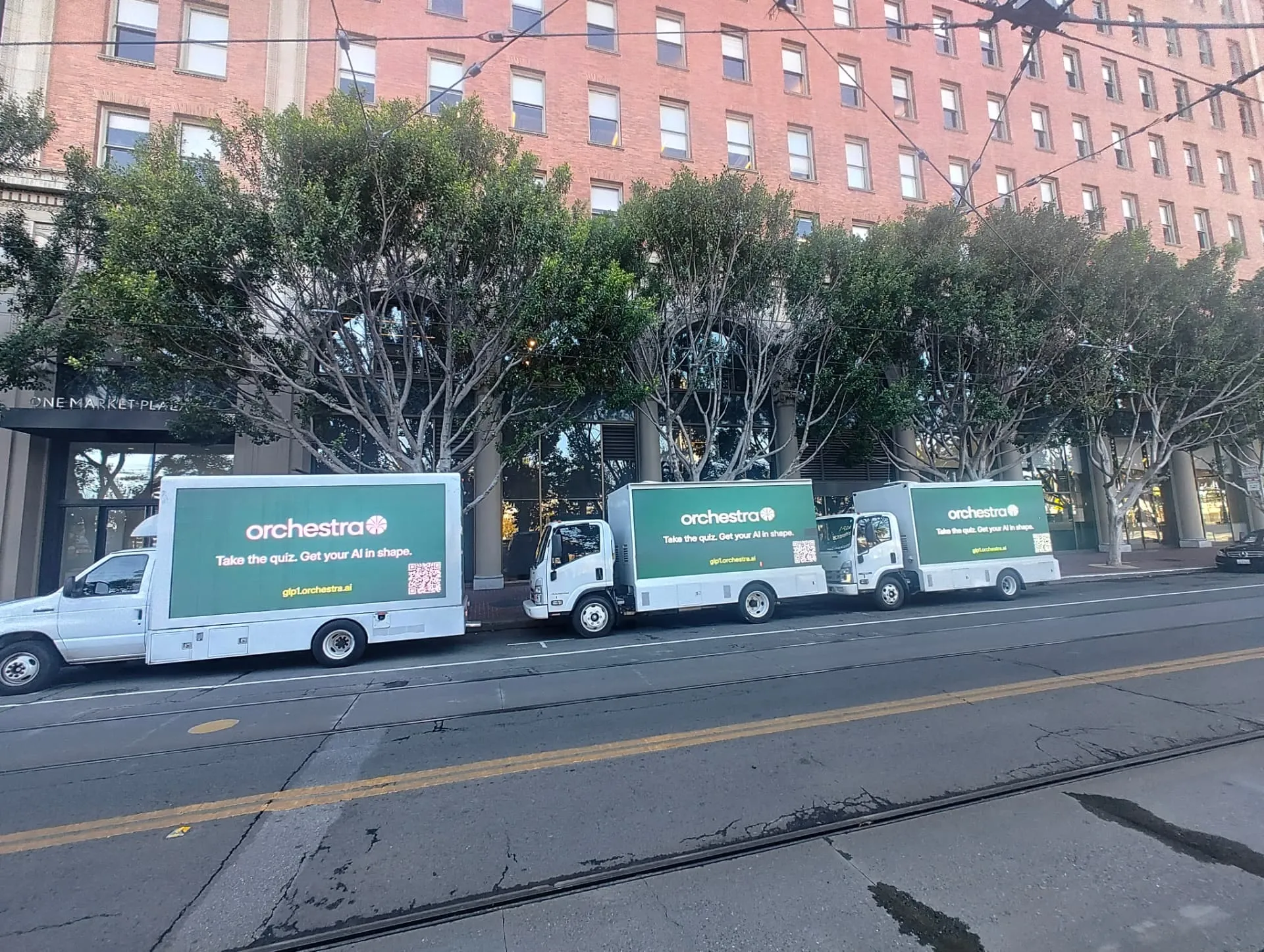 Three Orchestra AI LED billboard trucks displaying matching green creative outside One Market in San Francisco