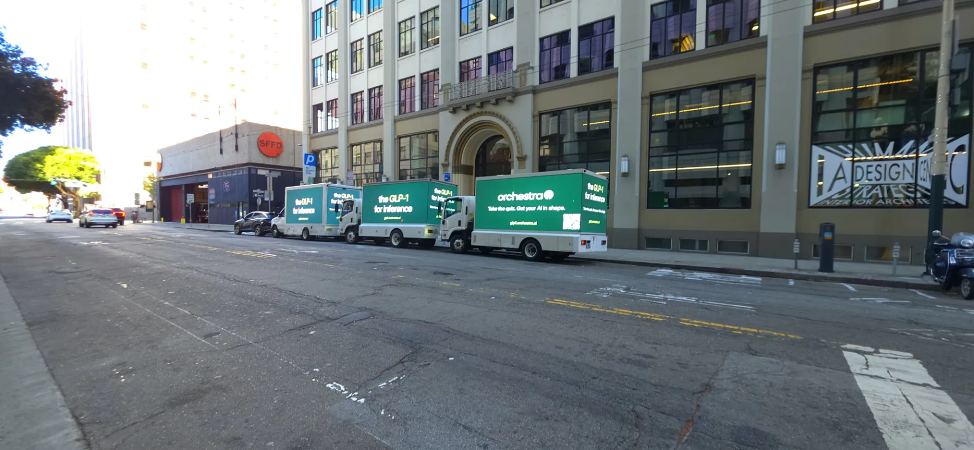 Wide San Francisco street view of three Orchestra AI LED billboard trucks lined up beside a building and SFFD entrance
