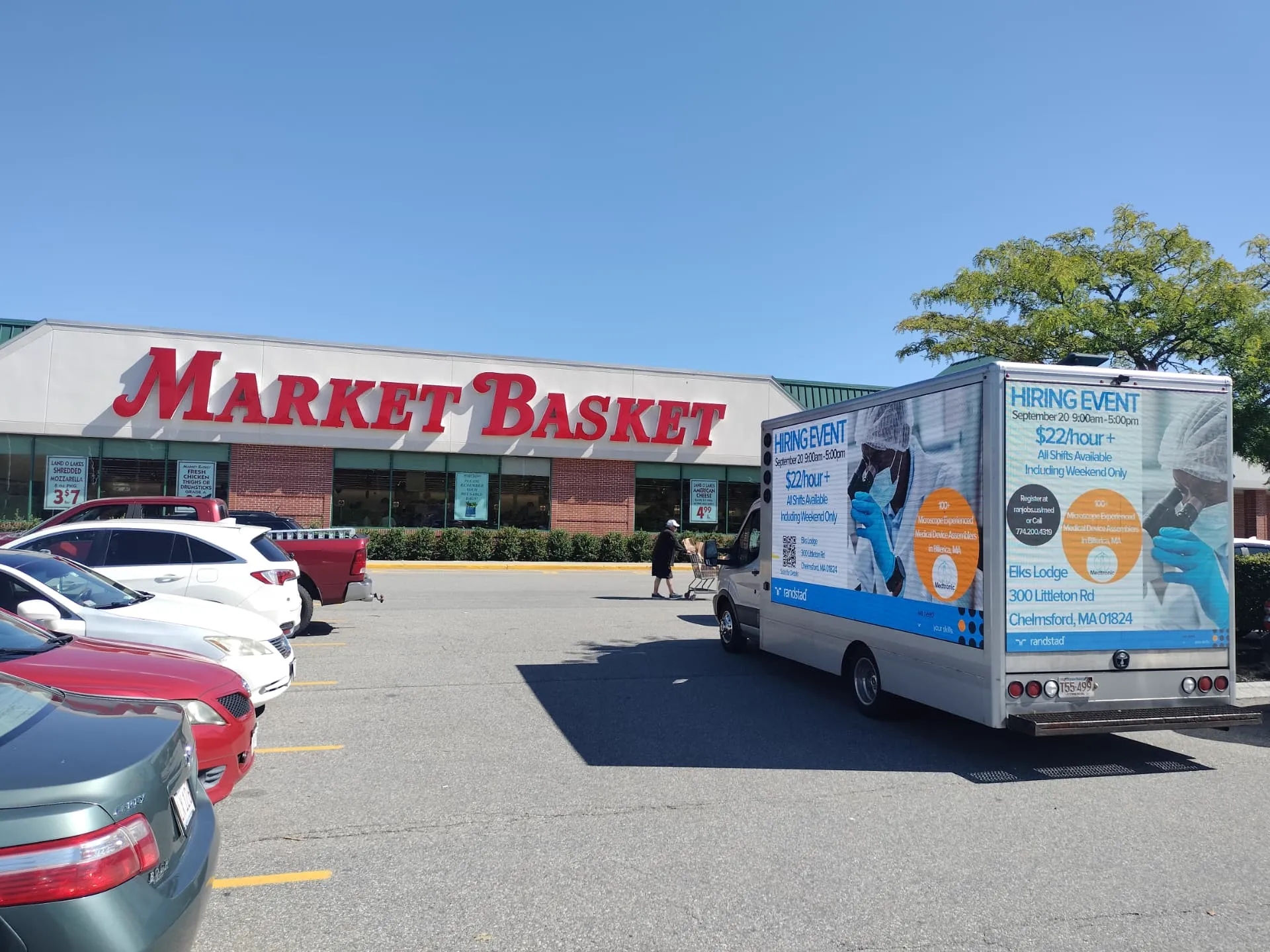 Mobile LED billboard truck promoting a Randstad and Medtronic hiring event for microscope-experienced medical device assemblers outside Market Basket in Chelmsford, MA