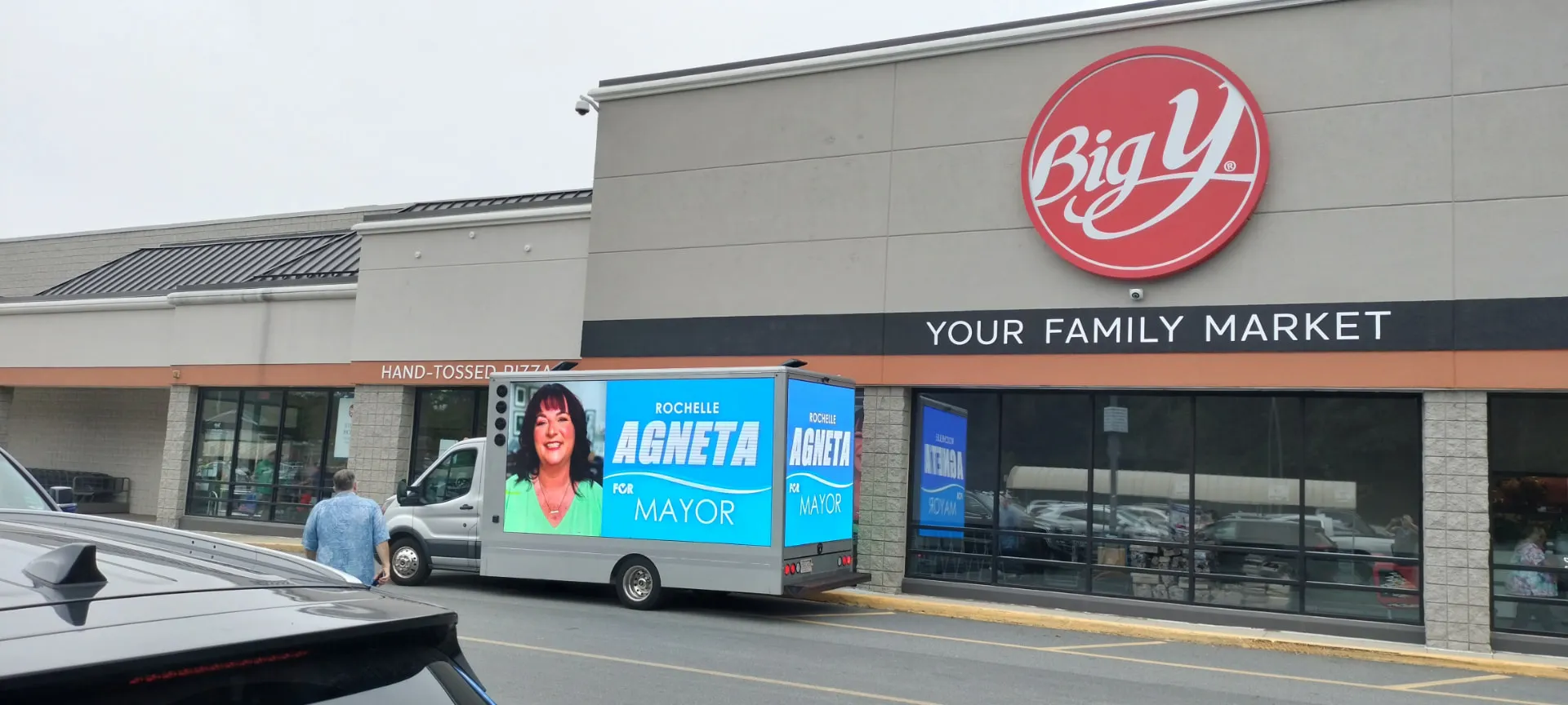 LED billboard truck displaying a candidate advertisement outside a busy grocery store entrance