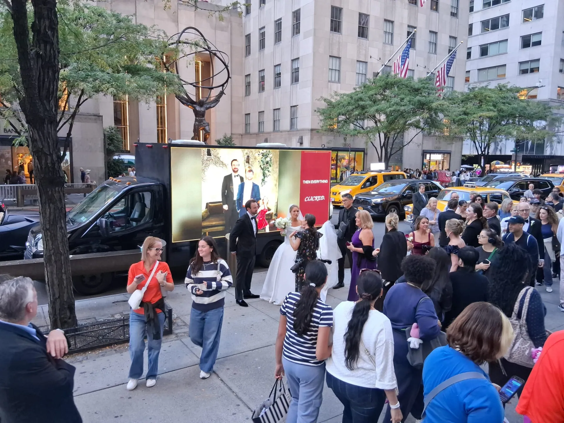 Wedding guests gathered around a mobile LED billboard truck displaying the couple's photos at Rockefeller Center NYC