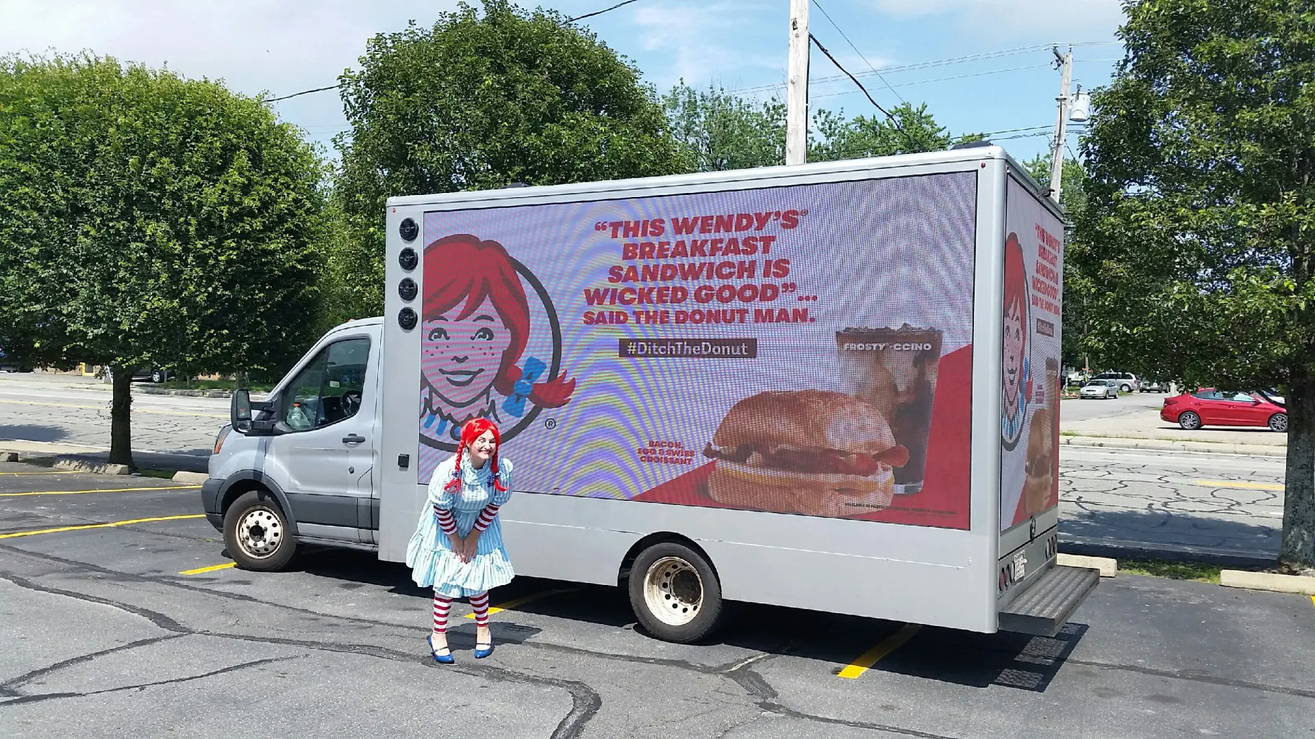 Wendy's LED billboard truck reading This Wendy's Breakfast Sandwich Is Wicked Good with the Wendy mascot in a parking lot